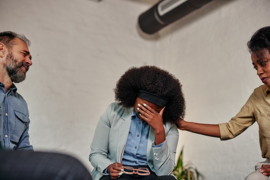 a woman with her hand on forehead while being comforted